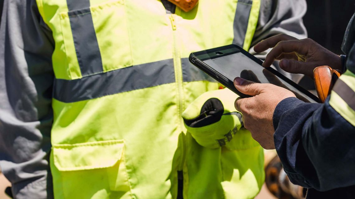 Two people in yellow safety vests looking at a tablet